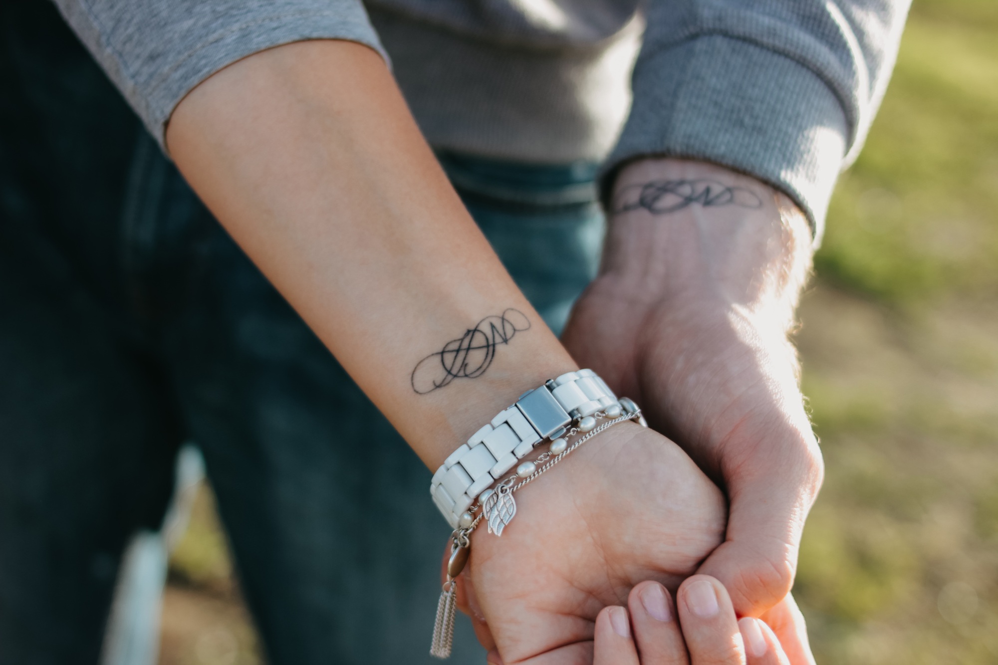 A couple in love holding hand in hand. Paired tattoo initials on the arms