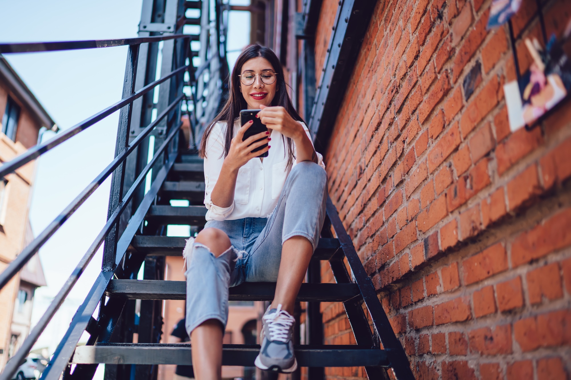 Cheerful female texting on smartphone on stairs