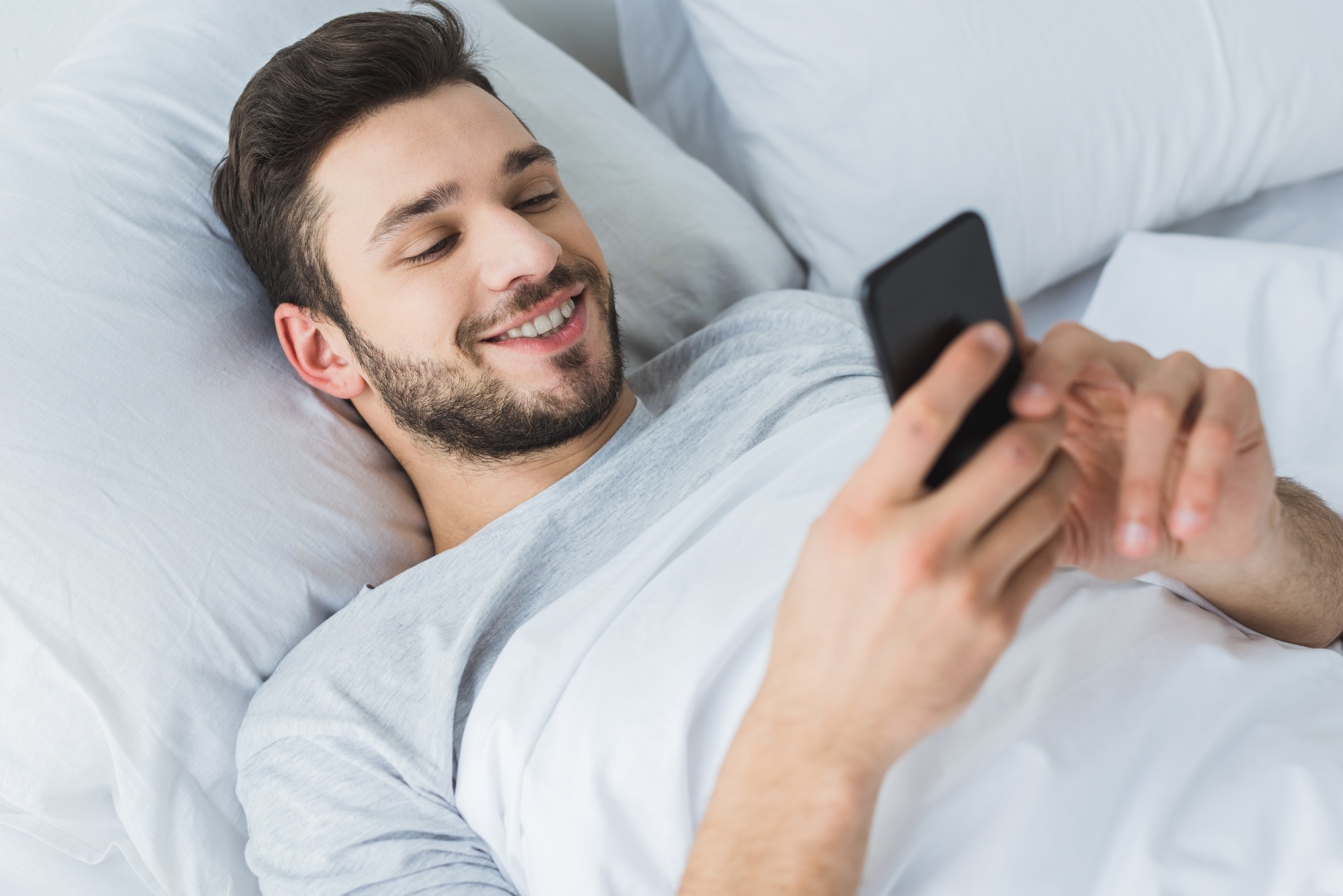 happy bearded man using smartphone in bed in the morning