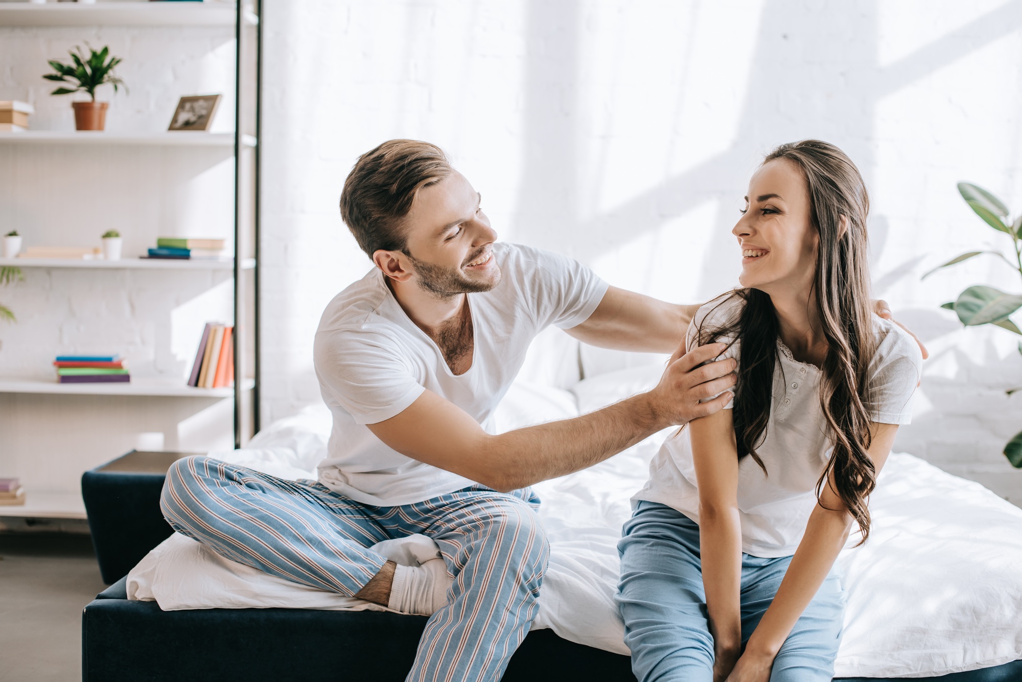 laughing young couple having fun while sitting on bed in morning