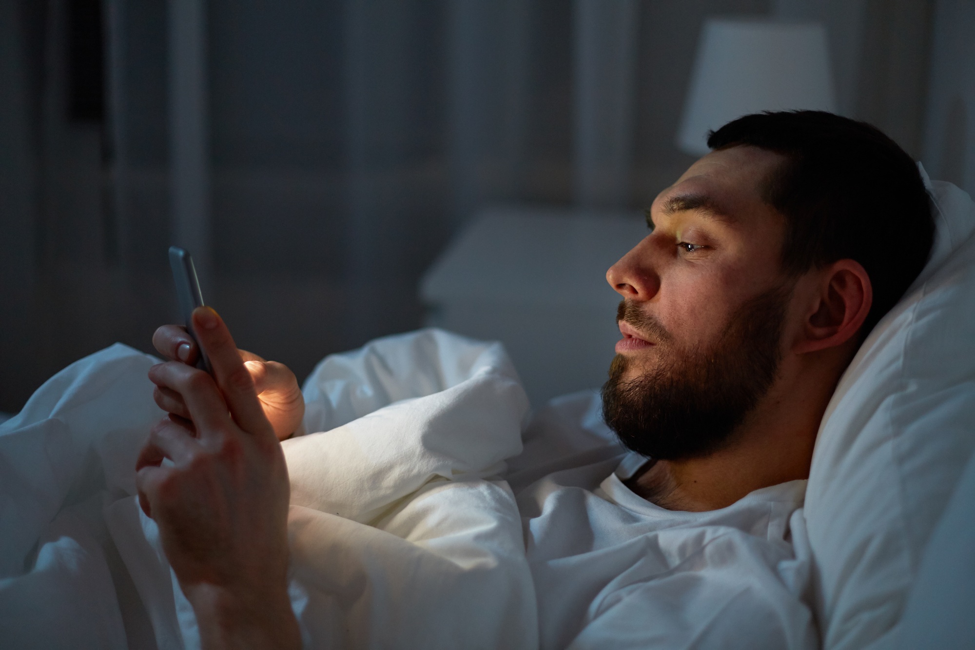 man with smartphone in bed at night