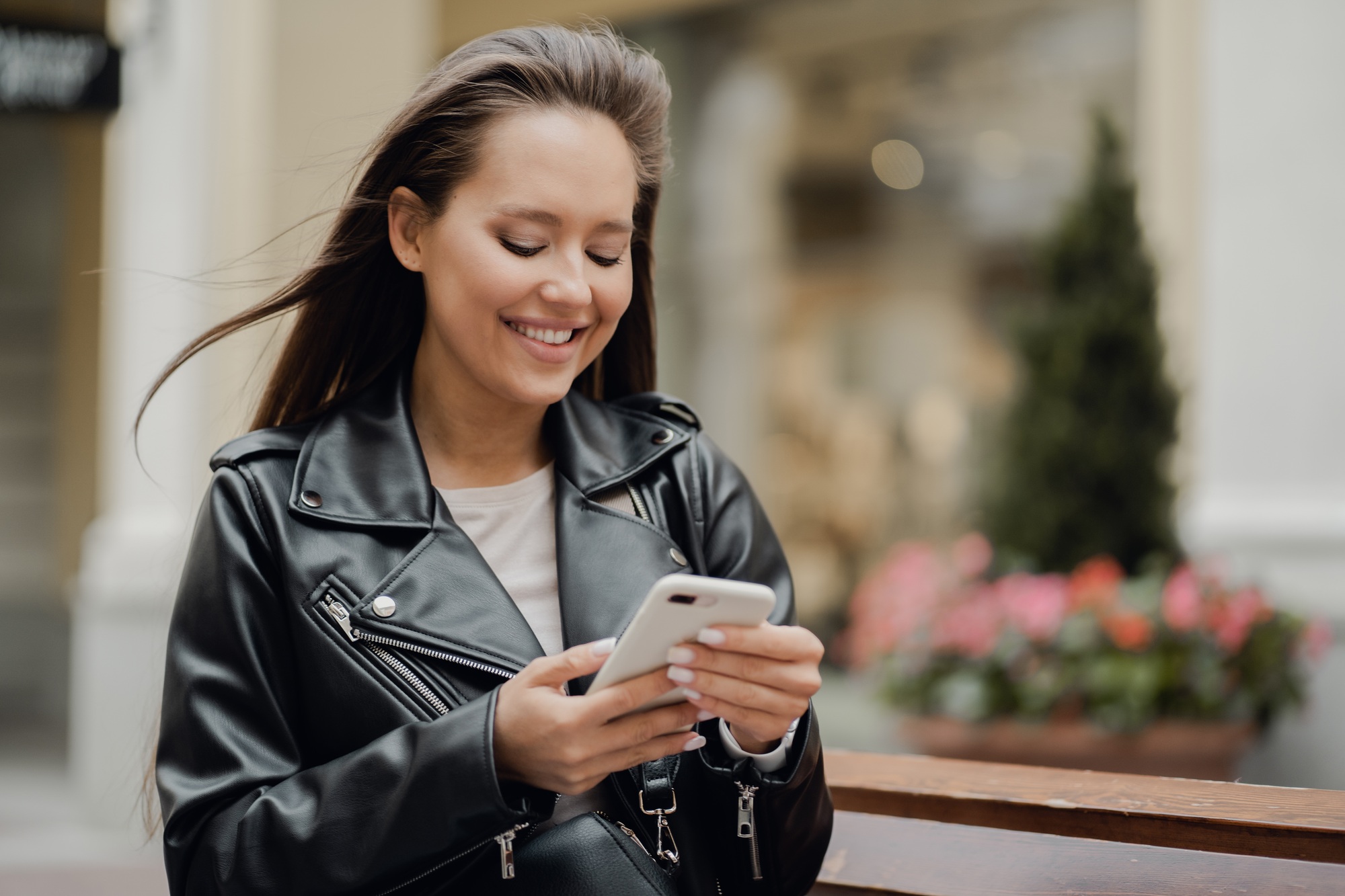 young girl writes sms on the phone to her friend, brunette smiles, good mood