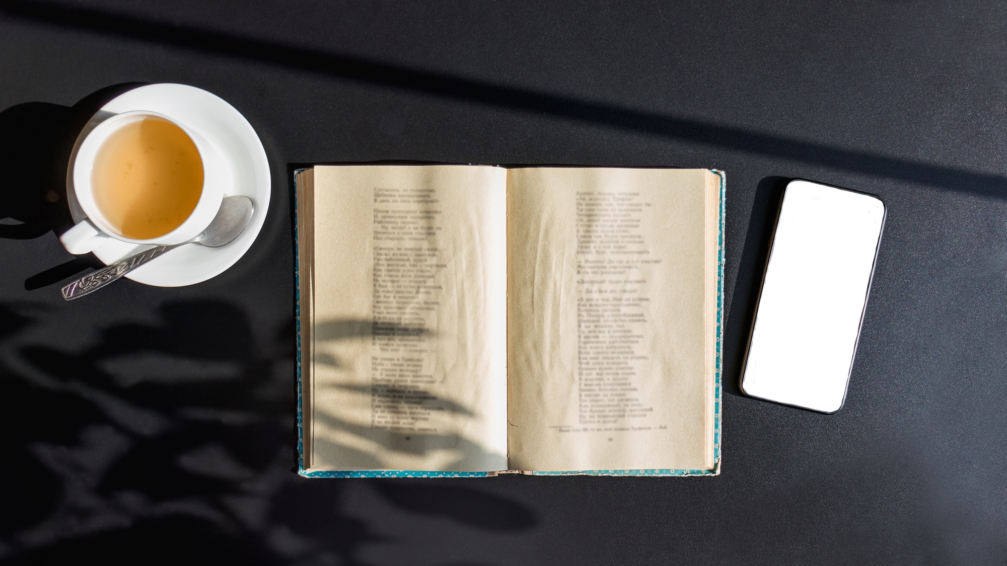book smartphone and focal of tea on black table, bright sun and hard shadows.love of reading