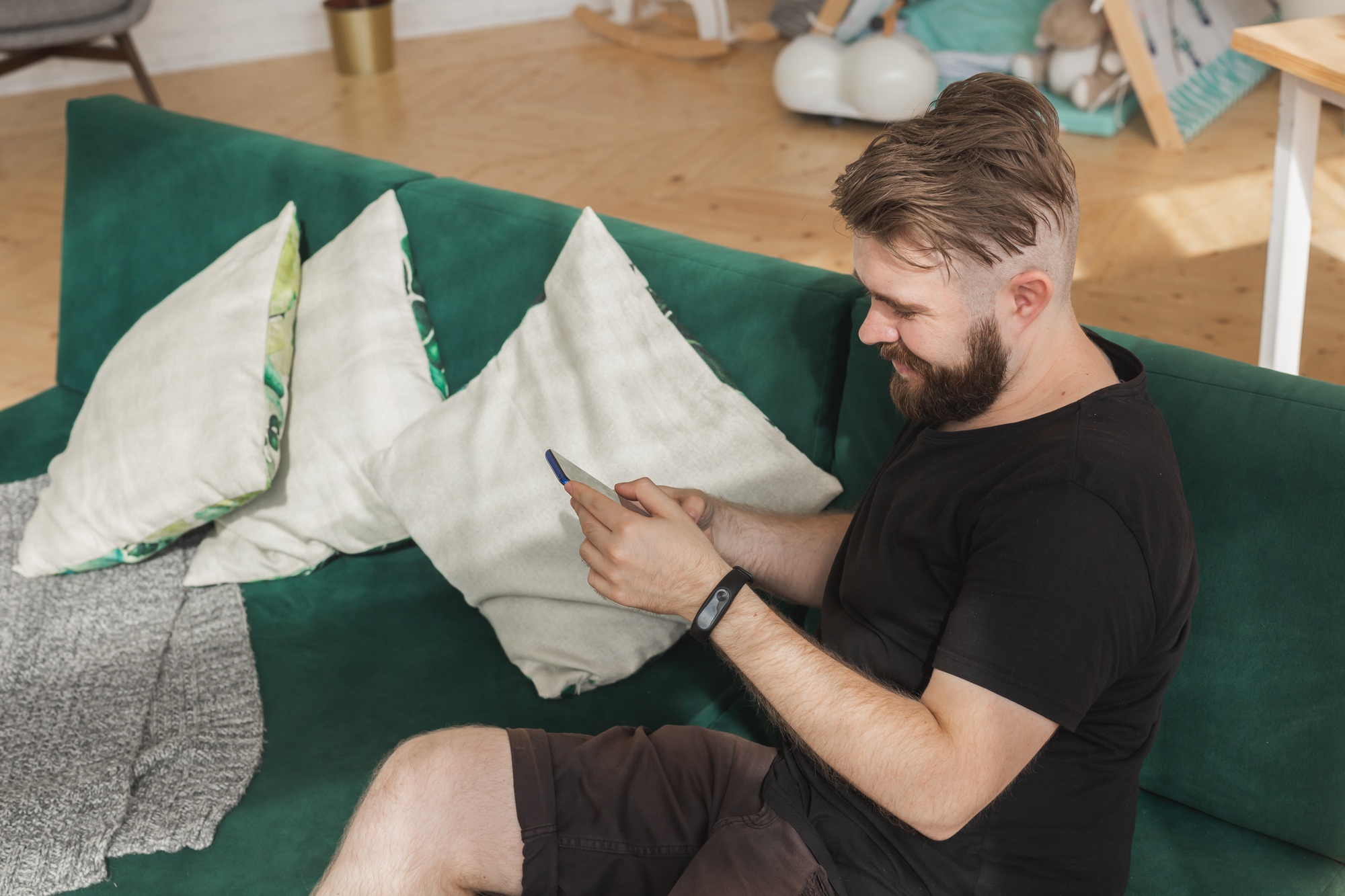 Relaxed man using a smartphone sitting on green couch in the living room at home